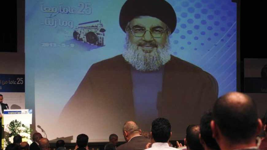 People applaud as Lebanon's Hezbollah leader Sayyed Hassan Nasrallah appears on a screen during a live broadcast to speak to his supporters at an event marking the 25th anniversary of the establishment of Al-Nour radio station, which is operated by the Hezbollah in Beirut, May 9, 2013. REUTERS/Sharif Karim (LEBANON - Tags: POLITICS MEDIA ANNIVERSARY) - RTXZGEQ