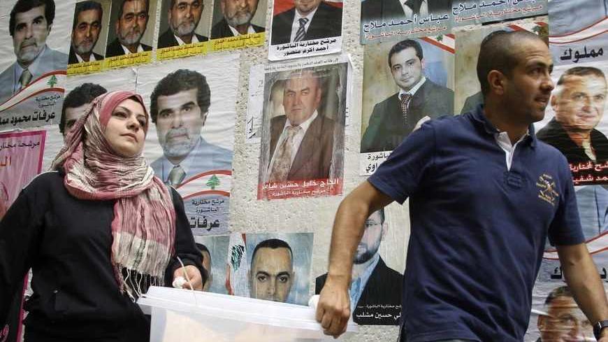 Lebanese government election officials walk past a wall on which posters of Lebanese candidates running in the country's municipal election are pasted, as they carry a ballot box ahead of the country's municipal elections, in Beirut May 8, 2010. The voting is spread across four regions, each of which will vote on a Sunday in May. Beirut will be the second region to vote on Sunday, May 9, 2010. REUTERS/Mohamed Azakir   (LEBANON - Tags: ELECTIONS POLITICS) - RTR2DLXT