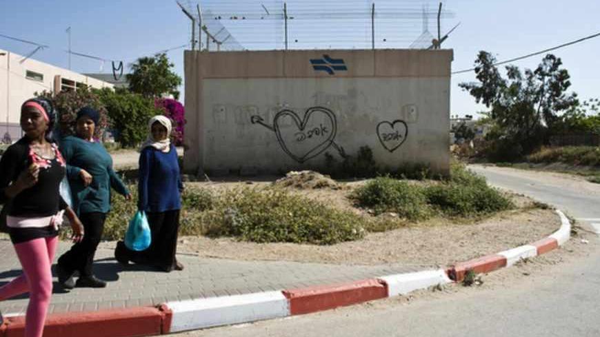 Women walk past a Hebrew graffiti that reads "Love" in the "Train" neighbourhood in Lod May 15, 2012. The backstreets of Lod, a mixed Arab-Jewish city just 20 minutes from the tree-lined boulevards of Tel Aviv, reveal a seamy underside of Israel that few visitors get to see, tucked away behind Ben Gurion airport off the main highway to Jerusalem and the occupied West Bank. Picture taken May 15, 2012. To match Feature ISRAEL-ARABS/CRIME        REUTERS/Nir Elias  (ISRAEL - Tags: SOCIETY) - RTR32TYI