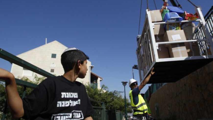 A boy watches as a crane lowers the belongings of families moving out of the Ulpana neighbourhood of the Beit El settlement June 26, 2012. Settlers on Tuesday began moving out of apartment blocs that Israel's Supreme Court ruled had been built illegally on Palestinian-owned land, after reaching an agreement with the government to go quietly. His  T-shirt reads, "Ulpana neighbourhood, will return".  REUTERS/Baz Ratner (WEST BANK - Tags: POLITICS RELIGION) - RTR3463H