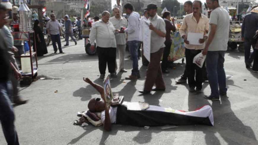 An anti-government protester, who is covered with an Egyptian flag, and has a model depicting a tank, holds a picture of former Egypt's President Gamal Abdel Nasser while lying down on the ground in Tahrir square during a demonstration in Cairo May 17, 2013. REUTERS/Asmaa Waguih (EGYPT - Tags: POLITICS CIVIL UNREST) - RTXZQNK