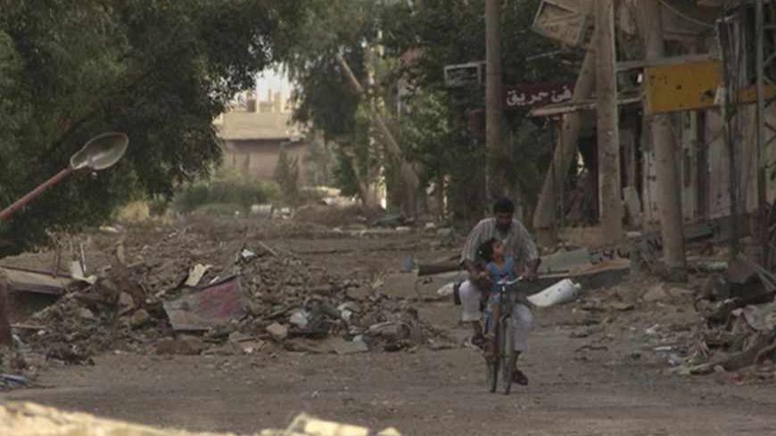 A man rides a bicycle with a child along a damaged street full of debris in Deir al-Zor May 19, 2013. Picture taken May 19, 2013. REUTERS/Khalil Ashawi (SYRIA - Tags: CONFLICT SOCIETY) - RTXZTR4