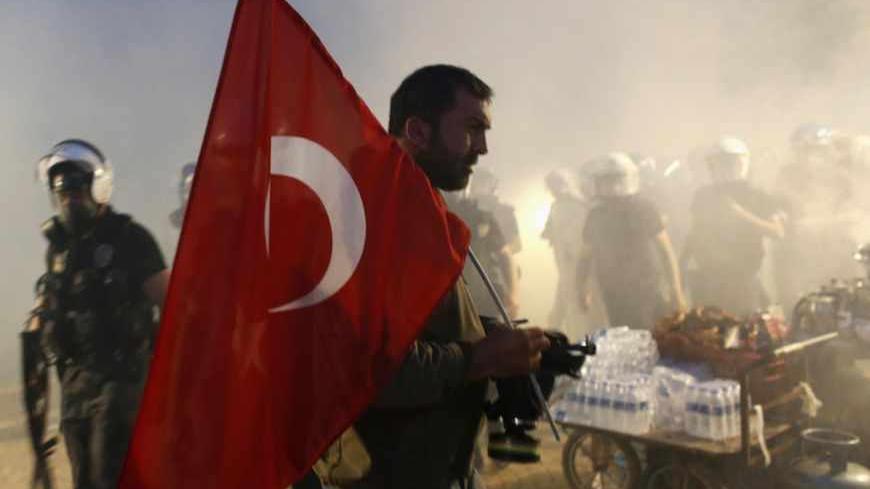 A protester holds a Turkish flag as riot police order them to evacuate Gezi Park in central Istanbul June 15, 2013. Thousands of people took to the streets of Istanbul overnight on Sunday, erecting barricades and starting bonfires, after riot police firing teargas and water cannon stormed a park at the centre of two weeks of anti-government unrest. Lines of police backed by armoured vehicles sealed off Taksim Square in the centre of the city as officers raided the adjoining Gezi Park late on Saturday, where