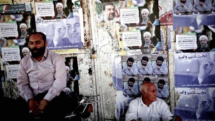 Iranians sit next to electoral posters of Hassan Rohani (L) and Mohsen Rezai (C) in the religious city of Qom some 130 kilometres south of the capital on June 9, 2013. Iran elects on June 14 a successor to President Mahmoud Ahmadinejad, whose eight years in office have been marked by stiff Western sanctions over Tehran's controversial nuclear drive and the economic turmoil they have caused. AFP PHOTO/BEHROUZ MEHRI        (Photo credit should read BEHROUZ MEHRI/AFP/Getty Images)