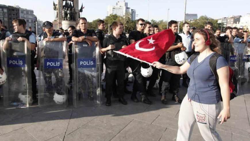 An anti-government protester waves a Turkish flag in front of riot police during a demonstration at Taksim square in central Istanbul June 25, 2013. Turkish anti-terrorism police detained 20 people in raids in the capital Ankara on Tuesday in connection with weeks of anti-government protests across the country, media reports said. The unrest began at the end of May when police used force against campaigners opposed to plans to redevelop a central Istanbul park. The protest spiralled into broader demonstrati