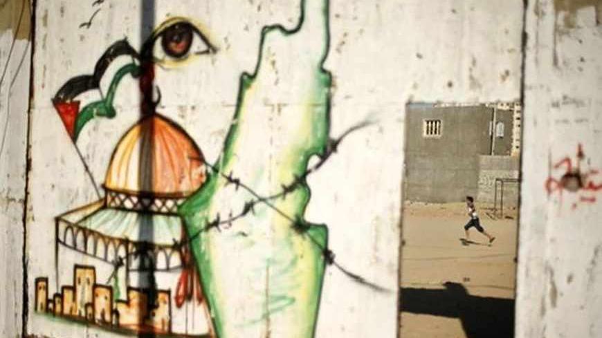 A Palestinian boy plays soccer as a mural depicts the Dome of the Rock and a map of British Mandate Palestine, on the gate of al-Sadaka club in Gaza City June 23, 2013. REUTERS/Mohammed Salem (GAZA - Tags: SOCIETY TPX IMAGES OF THE DAY) - RTX10YBI