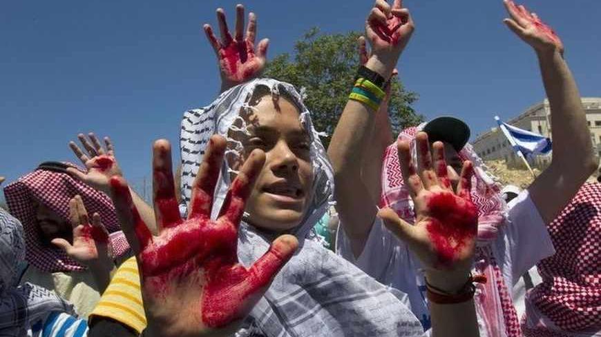Israelis wearing keffiyehs hold up hands covered in fake blood protest outside the office of Israel's Prime Minister Benjamin Netanyahu in Jerusalem, against the release of Arab prisoners as a step to renew stalled peace talks with the Palestinians, July 28, 2013. Netanyahu on Sunday urged divided rightists in his cabinet to approve the release of 104 Arab prisoners in order to restart peace talk with the Palestinians. REUTERS/Ronen Zvulun (JERUSALEM - Tags: POLITICS CIVIL UNREST) - RTX122BK