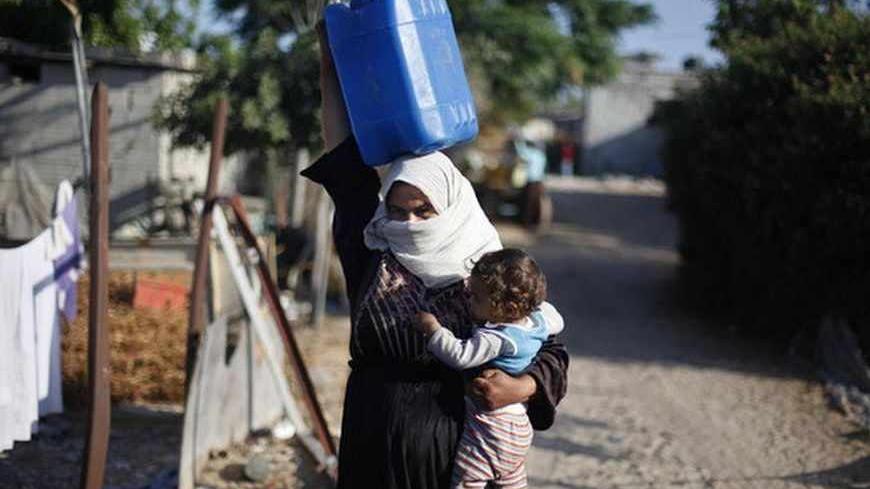 A Palestinian woman carries her daughter as she makes her way to fill a container with water from a nearby tank in Khan Younis in the southern Gaza Strip June 20, 2013. A tiny wedge of land jammed between Israel, Egypt and the Mediterranean sea, the Gaza Strip is heading inexorably into a water crisis that the United Nations says could make the Palestinian enclave unliveable in just a few years. Picture taken June 20, 2013. REUTERS/Ibraheem Abu Mustafa (GAZA - Tags: POLITICS SOCIETY ENERGY BUSINESS) - RTX11