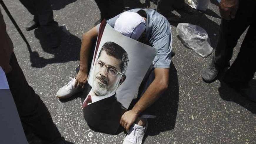 A member of the Muslim Brotherhood and supporter of ousted Egyptian President Mohamed Mursi with a poster of Mursi sits on the ground in front of the courthouse and the Attorney General's office during a demonstration in Cairo July 22, 2013. The family of ousted Egyptian President Mohamed Mursi said on Monday it would take legal action against the army, accusing it of abducting the country's first democratically-elected president. REUTERS/Amr Abdallah Dalsh  (EGYPT - Tags: POLITICS CIVIL UNREST RELIGION) - 