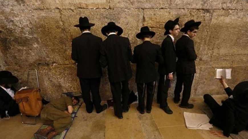 An Israeli soldier sleeps as ultra-Orthodox Jewish youths pray on Tisha B'Av at the Western Wall, Judaism's holiest prayer site, in Jerusalem's Old City July 16, 2013. Tisha B'Av, a day of fasting and lament, is traditionally the date in the Jewish calendar on which the First and Second Temples were destroyed, respectively in the sixth century B.C. by the Babylonians and the first century A.D. by the Romans. REUTERS/Baz Ratner (JERUSALEM - Tags: RELIGION TPX IMAGES OF THE DAY) - RTX11O0M