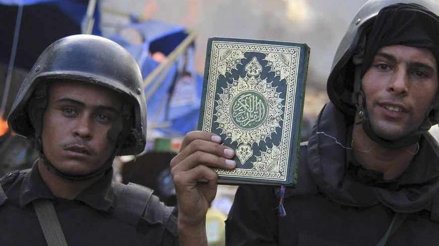 Riot police hold a copy of the Koran as they clear the area of members of the Muslim Brotherhood and supporters of deposed Egyptian President Mohamed Mursi, at Rabaa Adawiya square, where they are camping, in Cairo August 14, 2013. Egyptian security forces killed at least 30 people on Wednesday when they cleared a camp of Cairo protesters who were demanding the reinstatement of Mursi, his Muslim Brotherhood movement said. REUTERS/Stringer  (EGYPT - Tags: POLITICS CIVIL UNREST RELIGION) - RTX12KXZ