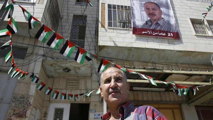 Jamil Nabi Annatsheh, a Palestinian prisoner freed by Israel, stands beneath a banner depicting him and hung outside his house in the West Bank city of Hebron August 14, 2013. Israeli and Palestinian negotiators were due to reconvene U.S.-brokered peace talks in Jerusalem on Wednesday amid little fanfare and low expectations, dogged by plans for more Jewish settler homes on occupied land. The resumption of negotiations, after a first round in Washington last month that ended a three-year standoff over Jewis