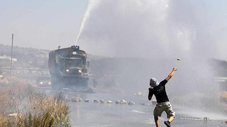 A Palestinian demonstrator hurls a stone as an Israeli truck fires a water cannon containing a foul smelling substance during clashes at a protest in the West Bank village of Nabi Saleh, near Ramallah September 14, 2012. The demonstrators were calling for an end to the Oslo accords, which were meant to pave the way to permanent peace with Israel. REUTERS/Mohamad Torokman (WEST BANK - Tags: POLITICS CIVIL UNREST) - RTR37YUV