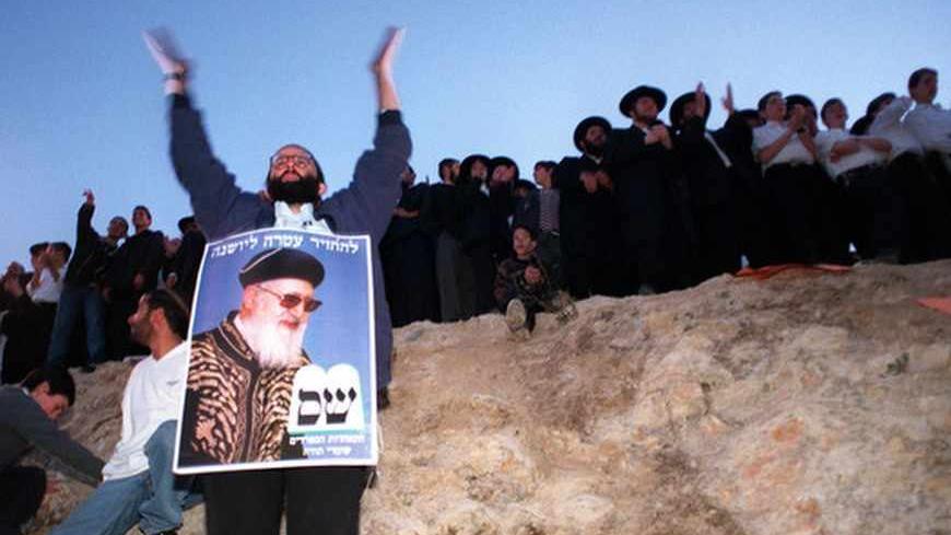 A Shas supporter, wearing a poster of Rabbi Ovadia Yosef the spiritual leader of the ultra-orthodox Shas party, joins thousands of other supporters outside the Rabbi's home March 27 after Israel's attorney-general ordered police to investigate the Rabbi on suspicion of incitement against a political adversary. [Shas' support is vital to Ehud Barak's hopes of making peace with Syria and the Palestinians. The police probe stems from remarks Yosef made about Education Minister Yossi Sarid, calling him a devil 