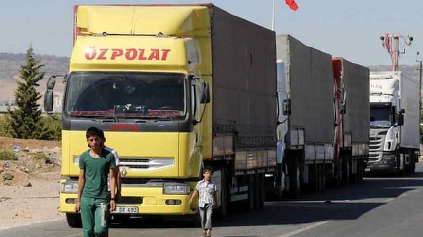 Locals walk past trucks lined up at the Oncupinar border crossing on the Turkish-Syrian border in the southeastern city of Kilis September 5, 2013. Every day, hundreds of trucks piled high with goods ranging from cooking oil to cement and nappies form queues stretching for miles at Oncupinar, now a bustling hub for trade with Syria. REUTERS/Umit Bektas (TURKEY - Tags: POLITICS BUSINESS CIVIL UNREST CONFLICT) - RTX1389O
