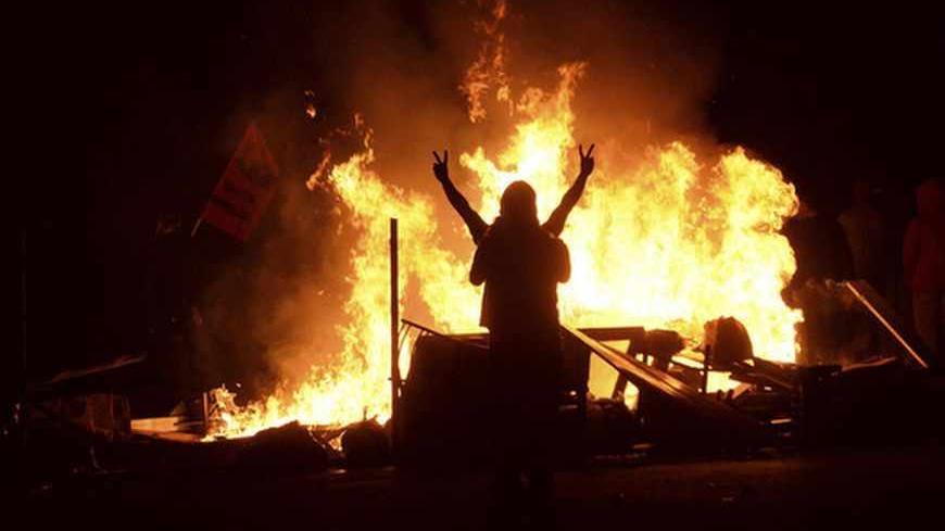 A demonstrator gestures as he stands behind burning barricades during a protest in the Tuzlucayir neighbourhood of Ankara September 9, 2013. Billed as a symbol of peace between two faiths, a new place of worship has turned Tuzlucayir, a poor suburb of Ankara, into a battleground and exposed wider sectarian tensions within Turkey. The project's blueprint envisages a Sunni mosque rising side by side with a new cemevi, or assembly house, to be used by Alevis, Turkey's biggest religious minority. But with its c