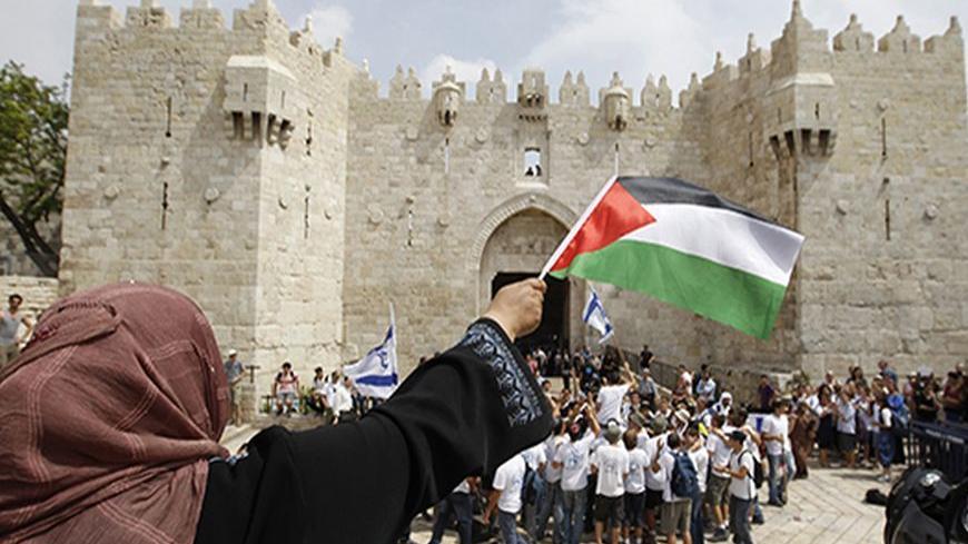 A Palestinian woman waves a Palestinian flag as Israeli youths celebrating Jerusalem Day dance in front of the Damascus Gate in Jerusalem's Old City May 8, 2013. On Wednesday Israel marks Jerusalem Day to celebrate the anniversary of its capture of the Eastern part of the city during the 1967 Middle East War. In 1980, Israel's parliament passed a law declaring united Jerusalem as the national capital, a move never recognised internationally. REUTERS/Ammar Awad (JERUSALEM - Tags: POLITICS CIVIL UNREST) - RTX