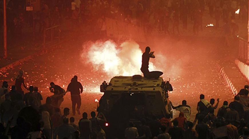A riot police officer, on a armoured personnel carrier surrounded by anti-Mursi protesters (foreground), fires rubber bullets at members of the Muslim Brotherhood and supporters of ousted Egyptian President Mohamed Mursi along a road at Ramsis square, which leads to Tahrir Square, during clashes at a celebration marking Egypt's 1973 war with Israel, in Cairo October 6, 2013. At least 28 people were killed and more than 90 wounded in clashes during protests in Egypt on Sunday, security sources and state medi