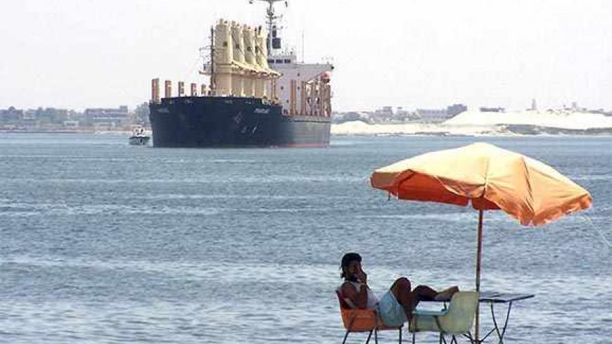 A man sits near a ship crossing the Suez Canal near Ismailia port city, 120 km (75 miles) northeast of Cairo, June 13, 2013. Revenue from Egypt's Suez Canal rose 1 percent in May from a year earlier to $438.1 million, Egypt's State Information Portal said on Thursday. REUTERS/Stringer  (EGYPT - Tags: MARITIME BUSINESS) - RTX10M8S
