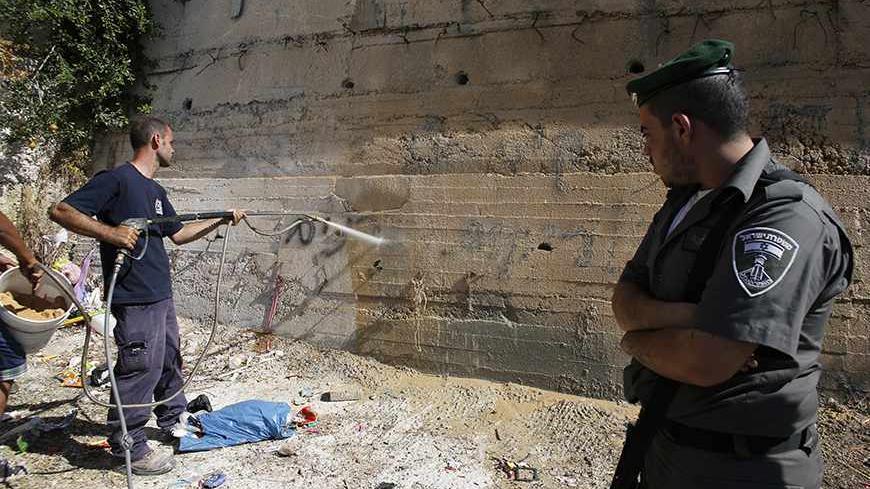 A Israeli border police officer looks as a municipality worker washes off graffiti sprayed on a wall in the Arab neighborhood of Beit Hanina in East Jerusalem June 24, 2013. Graffiti was sprayed and tires were slashed on 21 cars overnight in Beit Hanina in what appeared to be another in a series of "Price Tag" attacks by suspected Jewish militants. Police opened an investigation. The graffiti read: "We will not remain silent in the face of the stone-throwing". REUTERS/Ammar Awad (JERUSALEM - Tags: POLITICS 