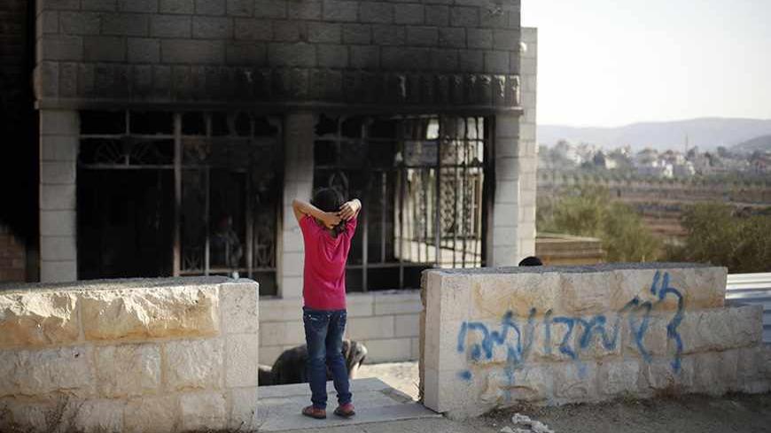 A Palestinian girl stands outside her torched house next to graffiti spray-painted on an outside wall of the home, in the West Bank village of Sinjil, near Ramallah November 14, 2013. Israeli settlers set fire to a Palestinian house on Thursday, leaving behind a message saying they were avenging the death of Eden Attias, an Israeli soldier killed by a Palestinian the previous day, residents said. The graffiti reads "Regards to Eden, Revenge!." REUTERS/Mohamad Torokman (WEST BANK - Tags: POLITICS CIVIL UNRES