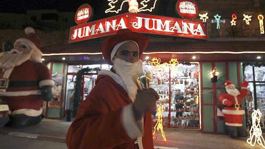 A Palestinian man dressed as Santa Claus rings a bell as he stands outside a shop in the West Bank city of Bethlehem December 23, 2007. Bethlehem is about to celebrate its most peaceful -- and profitable -- Christmas since 2000. Tourist levels are the best in seven years, with more than 60,000 people visiting last month compared to about 20,000 a year ago. REUTERS/Ammar Awad (WEST BANK) - RTX4Z3F