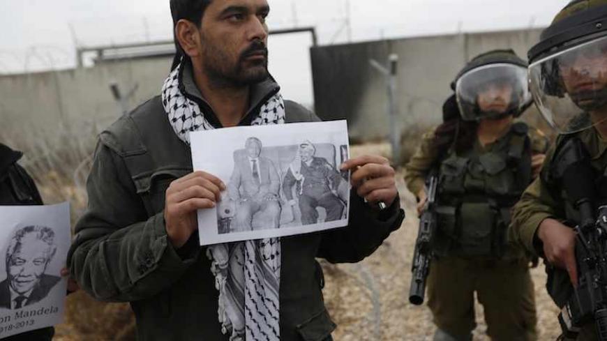 A Palestinian protester holds a placard depicting former South African President Nelson Mandela (L) and former Palestinian leader Yasser Arafat, as he stands near Israeli soldiers at a weekly demonstration against Jewish settlements in the West Bank village of Bilin, near Ramallah December 6, 2013. South African anti-apartheid hero Mandela died peacefully at home at the age of 95 on Thursday after months fighting a lung infection, leaving his nation and the world in mourning for a man revered as a moral gia