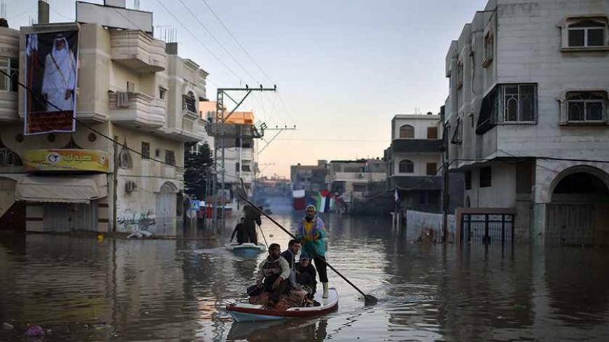 Palestinian civil defence volunteers paddle a boat to evacuate people from their houses that are flooded with rainwater as a poster depicting Qatar's Emir Sheikh Tamim bin Hamad is seen on a building, in the northern Gaza Strip December 16, 2013. Israel allowed the entry of 450,000 litres of fuel, paid for by Qatar, into the Gaza Strip on Sunday to enable the Palestinian territory's sole power plant to resume operations. Qatar answered an appeal by Gaza's government, led by the Islamist Hamas group, after f