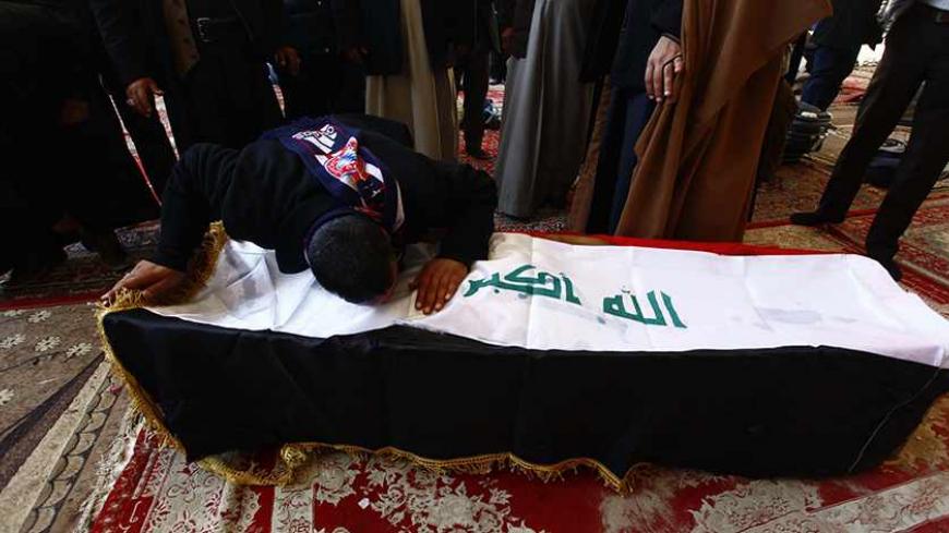 A man reacts on a coffin of his relative, who was killed in an attack in the western town of Rutba in Anbar province, during a funeral in Najaf, 160 km (100 miles) south of Baghdad, December 22, 2013. Militants killed at least 18 Iraqi officers and soldiers in Sunni-dominated Anbar province on Saturday, including a commander who oversaw a crackdown on Sunni protesters earlier this year, military sources said. REUTERS/Alaa Al-Marjani (IRAQ - Tags: CIVIL UNREST RELIGION POLITICS) - RTX16RMF