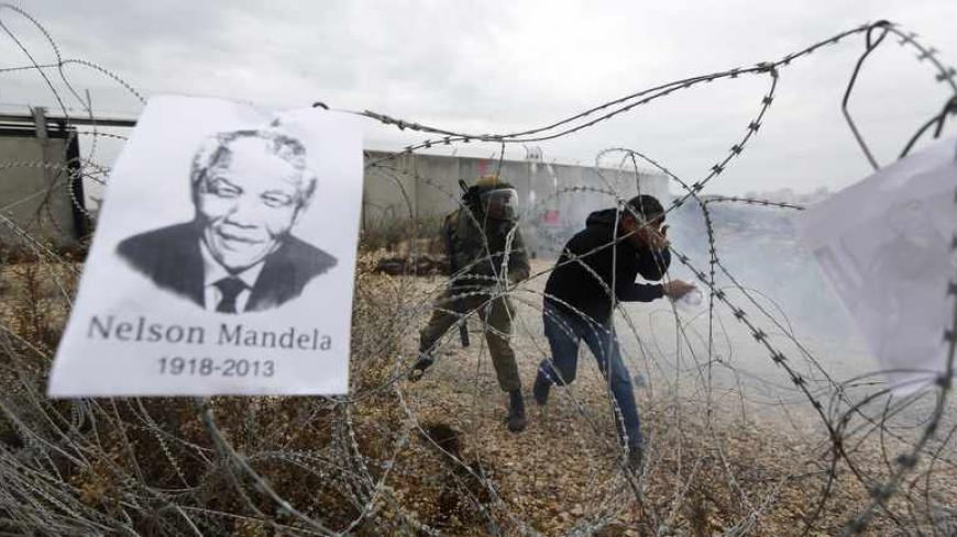 A placard depicting former South African President Nelson Mandela hangs on a barbed wire as a Palestinian protester reacts to tear gas fired by Israeli soldiers during clashes at a weekly demonstration against Jewish settlements in the West Bank village of Bilin, near Ramallah December 6, 2013. South African anti-apartheid hero Mandela died peacefully at home at the age of 95 on Thursday after months fighting a lung infection, leaving his nation and the world in mourning for a man revered as a moral giant. 