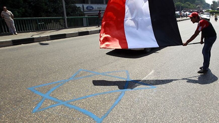 A protester waves an Egyptian flag above a Star of David symbol painted on the road during a protest in front of the Israeli embassy in Cairo August 19, 2011. Protesters gathered in front of the Israeli embassy to protest against Israel over the death of an Egyptian army officer and two security personnel who were killed during an Israeli raid on militants along the Egyptian Israeli border on Thursday.  REUTERS/Amr Abdallah Dalsh  (EGYPT - Tags: CIVIL UNREST POLITICS) - RTR2Q3SX