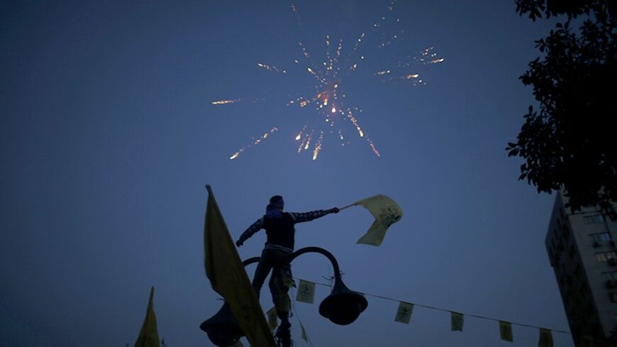 Fireworks are seen as a Palestinian waves a Fatah flag to celebrate the new year and the 49th anniversary of the founding of the Fatah movement, in Gaza City December 31, 2013.  REUTERS/Mohammed Salem (GAZA - Tags: POLITICS SOCIETY ANNIVERSARY) - RTX16Y3H
