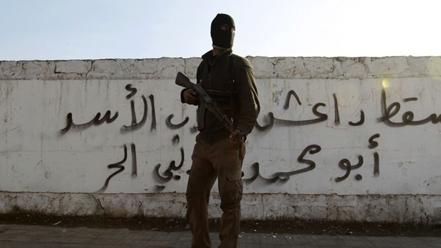 A Free Syrian Army fighter carries his weapon as he stands in front of graffiti that reads  "Daesh (Islamic State of Iraq and the Levant ) down" at Masaken Hanano neighborhood in Aleppo January 7, 2014. Five days of heavy rebel infighting has shaken the ISIL, which lost its main base in the northern city of Aleppo to rival rebels on Wednesday, according to a monitoring group. Picture taken January 7, 2014. REUTERS/Jalal Alhalabi (SYRIA - Tags: POLITICS CIVIL UNREST CONFLICT MILITARY) - RTX1767F