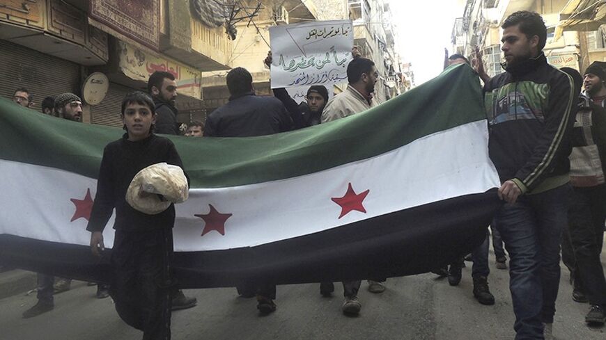 A boy holds bread as he walks in front of the Syrian opposition flag during a protest against Syria's President Bashar al-Assad and fighters from the Islamic State in Iraq and the Levant (ISIL) in Aleppo's Salaheddine neighbourhood January 10, 2014. REUTERS/Hosam Katan (SYRIA - Tags: POLITICS CIVIL UNREST CONFLICT) - RTX178MM