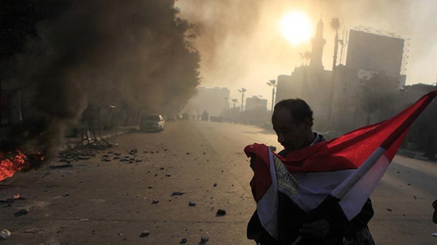 Anti-government protester holds a national flag during clashes at Ramsis street, which leads to Tahrir Square in downtown Cairo, on the third anniversary of Egypt's uprising, January 25, 2014. Seven people were killed during anti-government marches on Saturday while thousands rallied in support of the army-led authorities, underlining Egypt's volatile political fissures three years after the fall of autocrat president Hosni Mubarak. Security forces lobbed teargas and fired in the air to try to prevent demon