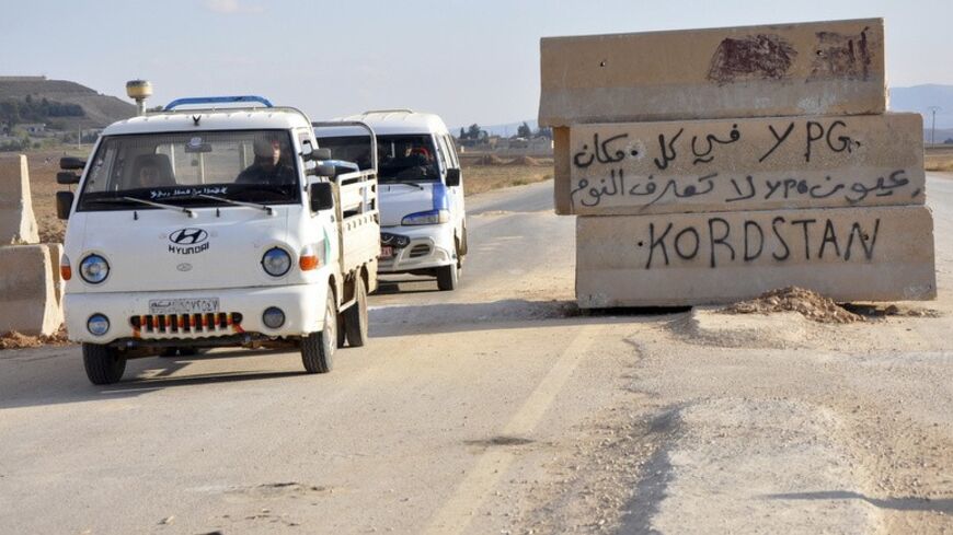 Vehicles pass a Kurdish People's Protection Units (YPG) checkpoint in Tell Tamer town in Hasaka, November 30, 2013. The text on the barrier reads in Arabic "YPG are everywhere, YPG don't sleep". Picture taken November 30, 2013. REUTERS/Rodi Said (SYRIA - Tags: POLITICS CIVIL UNREST CONFLICT) - RTX15ZU5