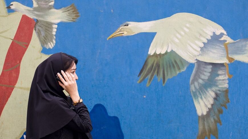 A woman talks on her mobile phone while passing a mural on a wall of the former U.S. embassy in Tehran November 5, 2008. REUTERS/Morteza Nikoubazl (IRAN) - RTXAA1D