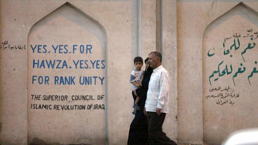 An Iraqi man and wife with child walk past a sign professing support for "Hawza," or Shiite religious leadership, 08 September 2003 in the holy city of Najaf, some 180 kms south of Baghdad. US President George W. Bush, in his first major speech on Iraq since May, urged the United Nations 07 September 2003 to overcome "past differences" over the US-led invasion of Iraq, appealing even to opponents of the war for troops and money.   AFP PHOTO/Karim SAHIB  (Photo credit should read KARIM SAHIB/AFP/Getty Images