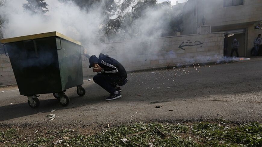 A stone throwing Palestinian hides behind a garbage bin as a tear gas canister fired by Israeli forces flies past him during clashes in the West Bank village of Birzeit, near Ramallah February 27, 2014. The clashes broke out after Israeli forces opened fire and killed a Palestinian they were seeking to arrest on Thursday, after the man had barricaded himself inside his house, Reuters witnesses said. An Israeli military statement said that Muataz Washaha, 24, had been wanted for "suspected terror activity" a