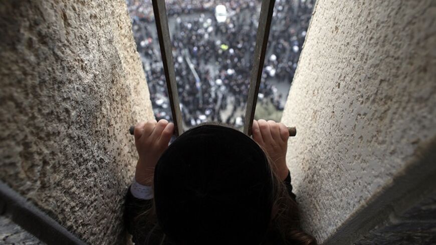 An ultra-Orthodox Jewish boy looks down from a balcony at a mass prayer in Jerusalem March 2, 2014. Hundreds of thousands of ultra-Orthodox Jews held a mass prayer in Jerusalem on Sunday in protest against a bill meant to slash military exemptions granted to seminary students, a tradition held since the founding of Israel. REUTERS/Darren Whiteside (JERUSALEM - Tags: POLITICS RELIGION MILITARY) - RTR3FWP4