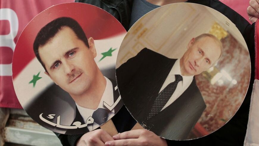 A participant hold images of Russian President Vladimir Putin and Syrian President Bashar al-Assad during an anti-war protest organised by the Communist party near the U.S. embassy in Moscow September 12, 2013. The banner in the background reads, "Mother Russia against war." REUTERS/Tatyana Makeyeva (RUSSIA - Tags: POLITICS CIVIL UNREST) - RTX13IXF