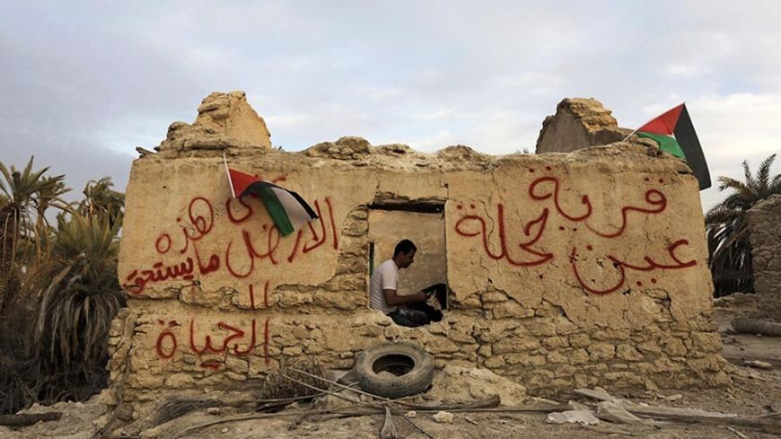 An Palestinian activist sits inside a structure in an old village known as Ein Hajla, in the Jordan Valley near the West Bank city of Jericho January 31, 2014. Some 100 Palestinian and foreign activists took part in a campaign to try to resettle the village and to protest Israel's occupation of the West Bank including the Jordan Valley. The graffiti on the wall reads "There is something worth living on this land for" (L) and "Ein Hajla village" (R). REUTERS/Ammar Awad (WEST BANK - Tags: POLITICS CIVIL UNRES
