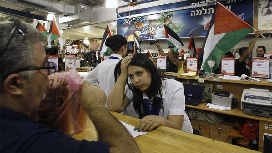 An Israeli worker holds her head as foreign and Palestinian activists holding Palestinian flags march through a supermarket in the West Bank Jewish settlement of Modiin Illit October 24, 2012. Some 50 activists marched through the supermarket and tried to block a road in the settlement on Wednesday during a protest against Jewish settlements and in a call to boycott settlement products. REUTERS/Ammar Awad (WEST BANK - Tags: POLITICS CIVIL UNREST FOOD) - RTR39INC