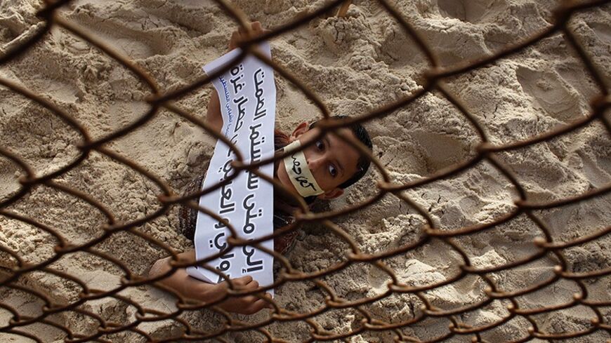 A Palestinian boy takes part in a protest against the blockade on Gaza, at the border between Egypt and Gaza Strip March 7, 2014. An Egyptian-Israeli blockade on the Gaza Strip, run by the Hamas Islamist movement, has left industry and construction gasping for resources, pushing unemployment to dizzying heights and deepening suffering for impoverished residents. The sign reads "How long will the international and Arab silence on Gaza blockade continue". REUTERS/Ibraheem Abu Mustafa (GAZA - Tags: POLITICS CI