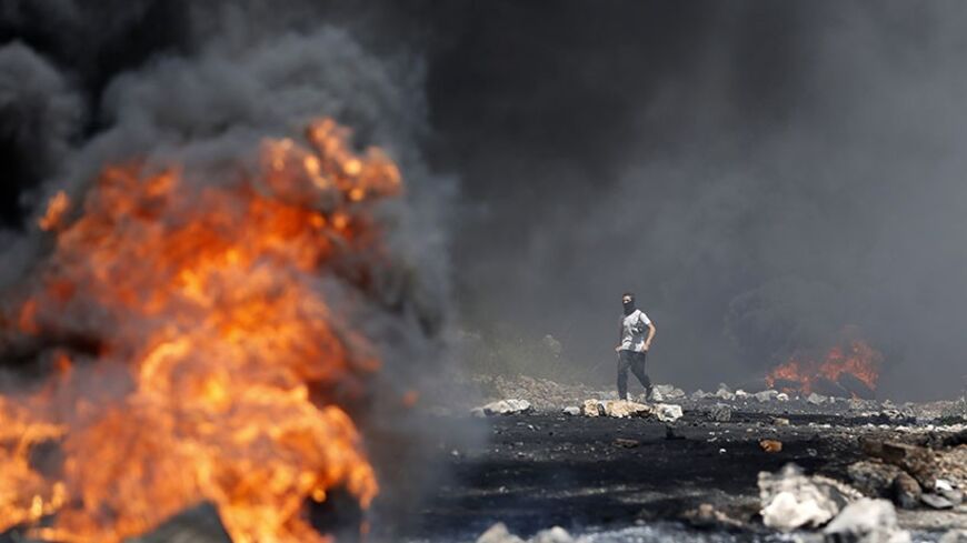 A masked Palestinian protester walks next to burning tyres during a weekly Friday protest against the Jewish settlement of Qadomem, near the West Bank City of Nablus April 25, 2014.  REUTERS/Mohamad Torokman (WEST BANK - Tags: POLITICS CIVIL UNREST TPX IMAGES OF THE DAY) - RTR3MMQK