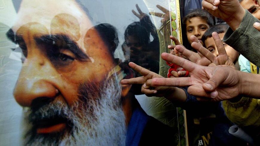 BAGHDAD, Iraq:  Supporters of the dominant Iraqi Shiite "United Iraqi Alliance" list flash the "V" sign near a picture of Grand Ayatollah Ali al-Sistani during a political rally in Baghdad's poor neighborhood of Sadr city, 12 December 2005. The United Iraqi Alliance list put on a show of force ahead of Iraqi elections for a full-term parliament, staging a rally that drew thousands in eastern Baghdad.  Iraqi violence shadowed special early polling Monday ahead of a general election for a full-term parliament