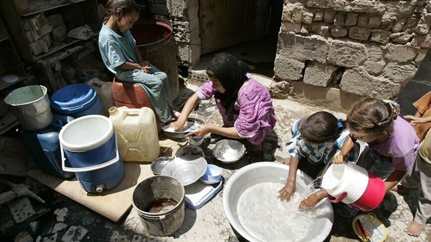 Girls wash dishes outside their house in a slum neighbourhood in Baghdad's Sadr City July 31, 2007. About 30 poor families make a living by gathering junk at the dumpsite in Sadr City, a vast slum in northeastern Baghdad.     REUTERS/Kareem Raheem (IRAQ) - RTR1SEUJ