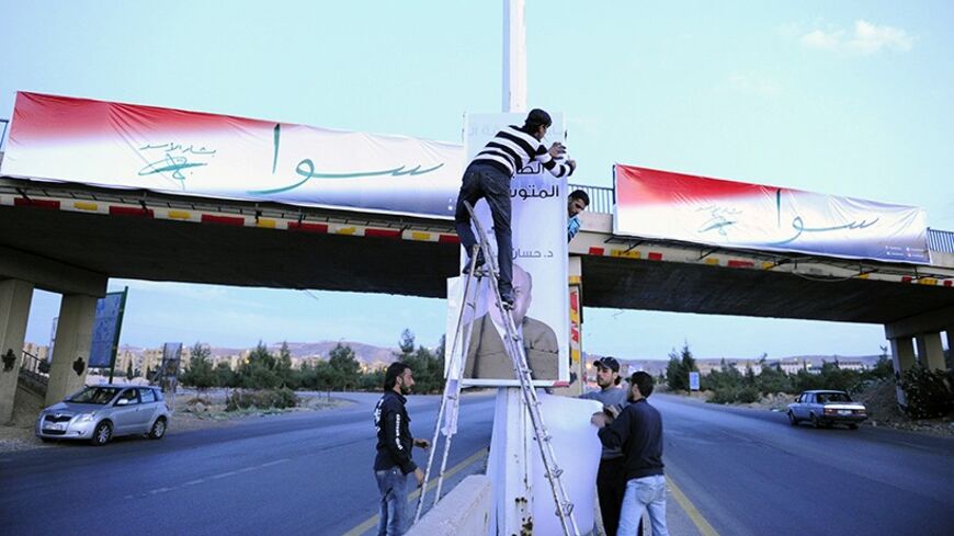 Workers hang banners for Hassan Abdallah al-Nouri in front of a banner for President Bashar al-Assad on a street in Damascus May 11, 2014.  Assad will compete with other two candidates in a June presidential election, the Supreme Constitutional Court of Syria said on Saturday. The poster consists of the Arabic word "Sawa" (Together) and Assad's name and signature (back) and "bringing back the middle class" with Dr. Hassan al-Nouri on the banner of his opponent (front). REUTERS/Omar Sanadiki  (SYRIA - Tags: 