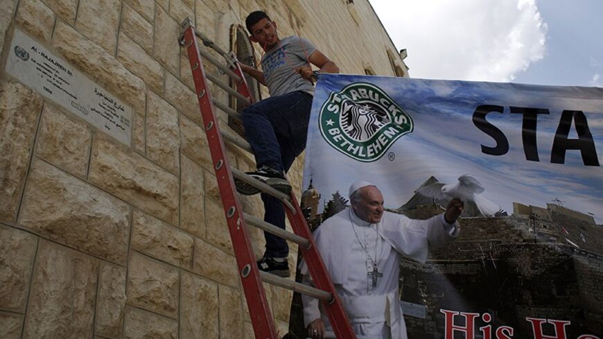 A Palestinian hangs a poster of Pope Francis in the West Bank town of Bethlehem May 22, 2014. With a Rabbi and a Muslim leader in tow, Pope Francis makes his first visit to the Middle East on Saturday, a delicate mission to push his vision of inter-religious dialogue as a vehicle for peace in the region. He will visit Jordan, the Palestinian Territories and Israel during his May 24-26 trip. REUTERS/Mohamad Torokman (WEST BANK - Tags: RELIGION POLITICS) - RTR3QD6G