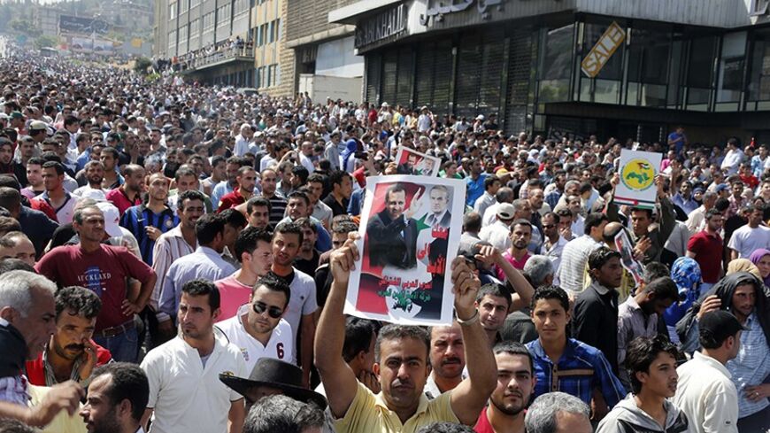 A Syrian national living in Beirut holds a picture of Syria's President Bashar al-Assad and his father, late President Hafez al-Assad, as Syrians gather to make their way to the Syrian Embassy in Beirut to cast their votes ahead of the June 3 presidential election, in Yarze, east of Beirut May 28, 2014. Expatriates and those who have fled the war were casting their ballots at dozens of Syrian embassies abroad ahead of next week's vote inside the country that opponents have dismissed as a farce as the fighti